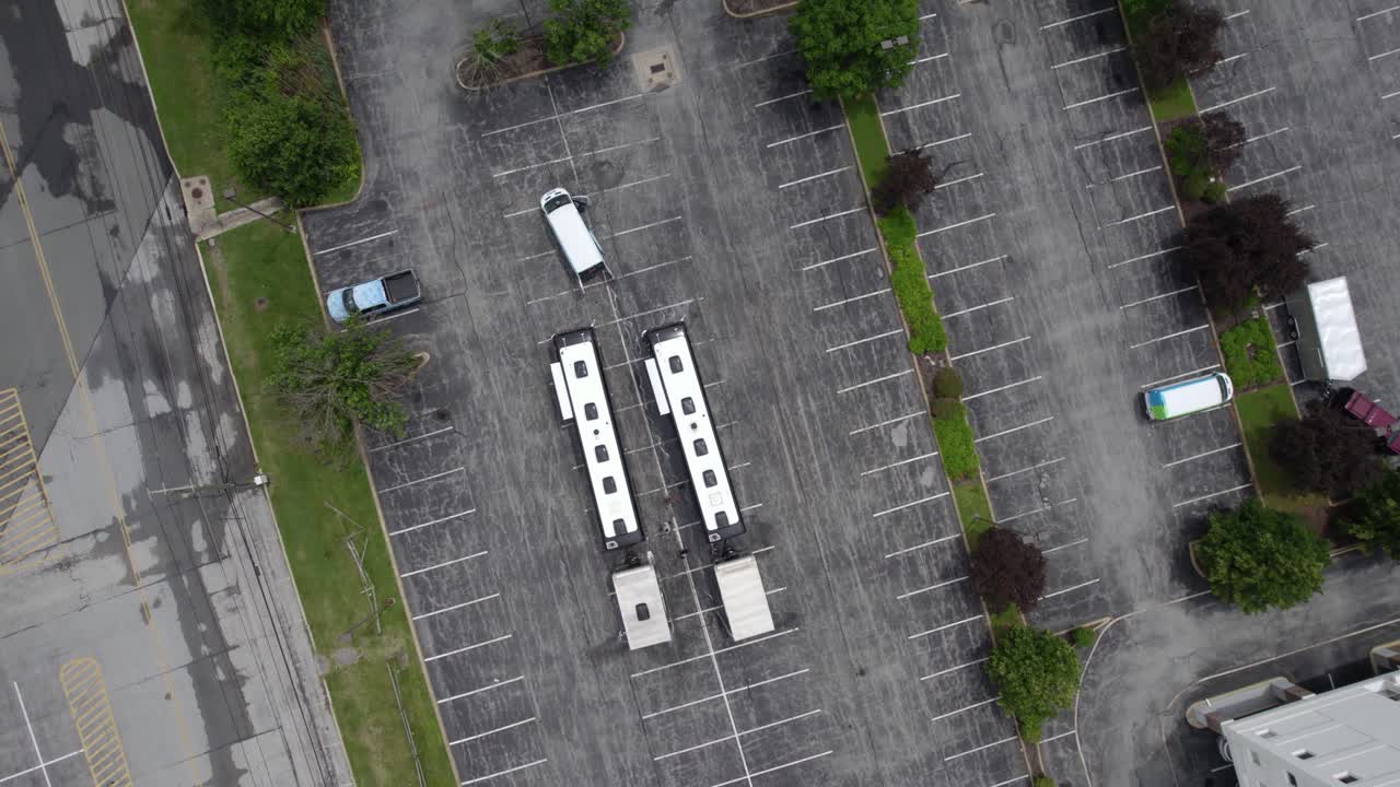 Aerial view above two tour buses with trailers on a parking lot - rotating, top down, drone shot