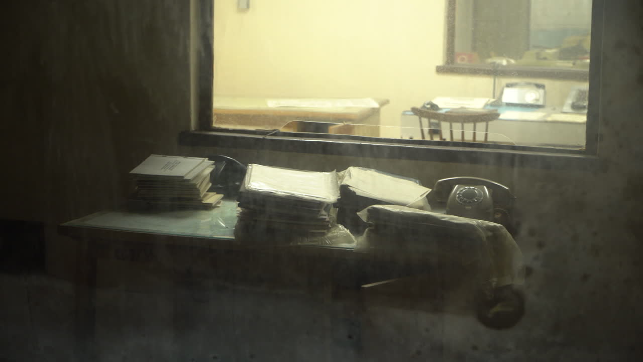 벙커 내부의 더러운 유리 뒤에 있는 오래된 빈티지 전화 및 종이 문서