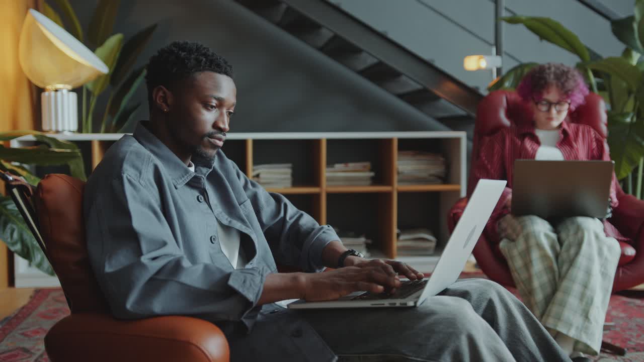 Black Man Browsing the Internet on Laptop in Armchair in Cozy Office