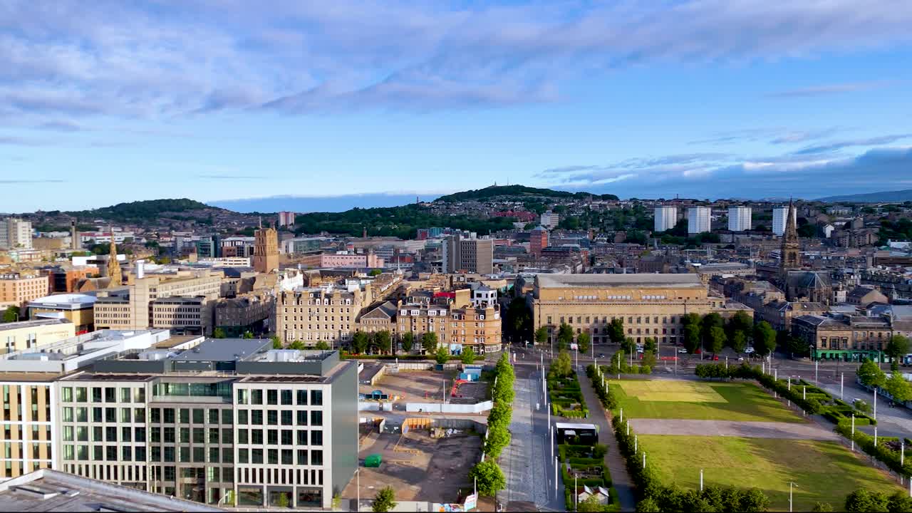 High-altitude drone footage smoothly pans across Inverness, Scotland, revealing urban architecture, green spaces, and distant hills under bright natural daylight