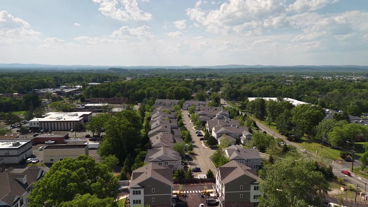 Vista aerea che avanza su un tranquillo quartiere residenziale suburbano con case e alberi verdi lussureggianti in una splendida giornata di sole, rivelando la città e il paesaggio in lontananza