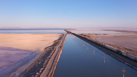drone vuela junto a un largo tren de carga que cruza la calzada sobre el gran lago salado en utah, ee.uu.