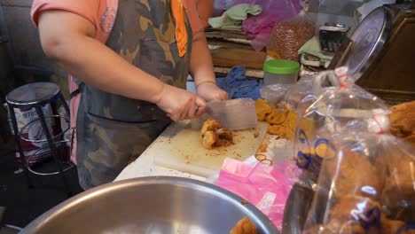 Asiatischer-Koch-Auf-Dem-Street-Food-Markt-Zerkleinert-Frittiertes-Schweinefleisch,-Verpackt-In-Plastiktüten-Am-Imbissstand