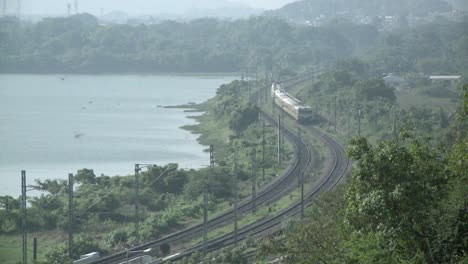 An-approaching-train-travels-a-rural-route-near-a-lake