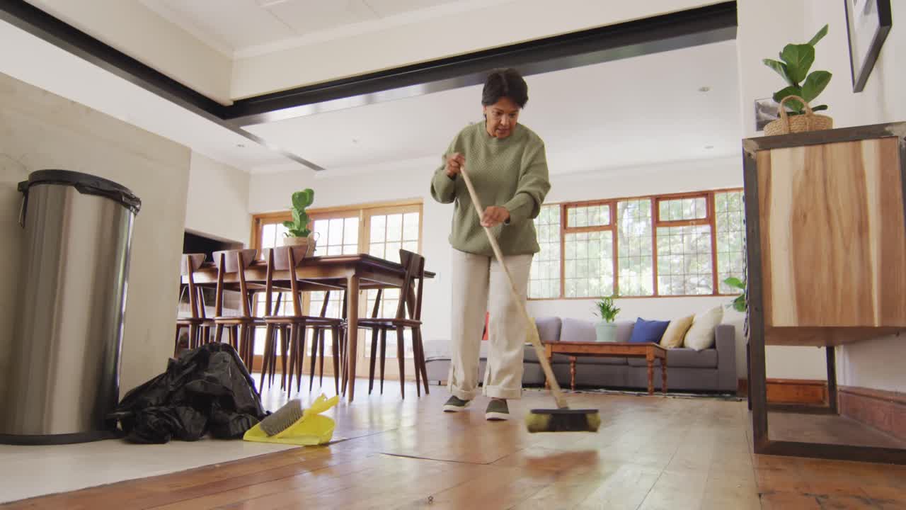 mujer asiática mayor limpiando el piso de la sala de estar en casa