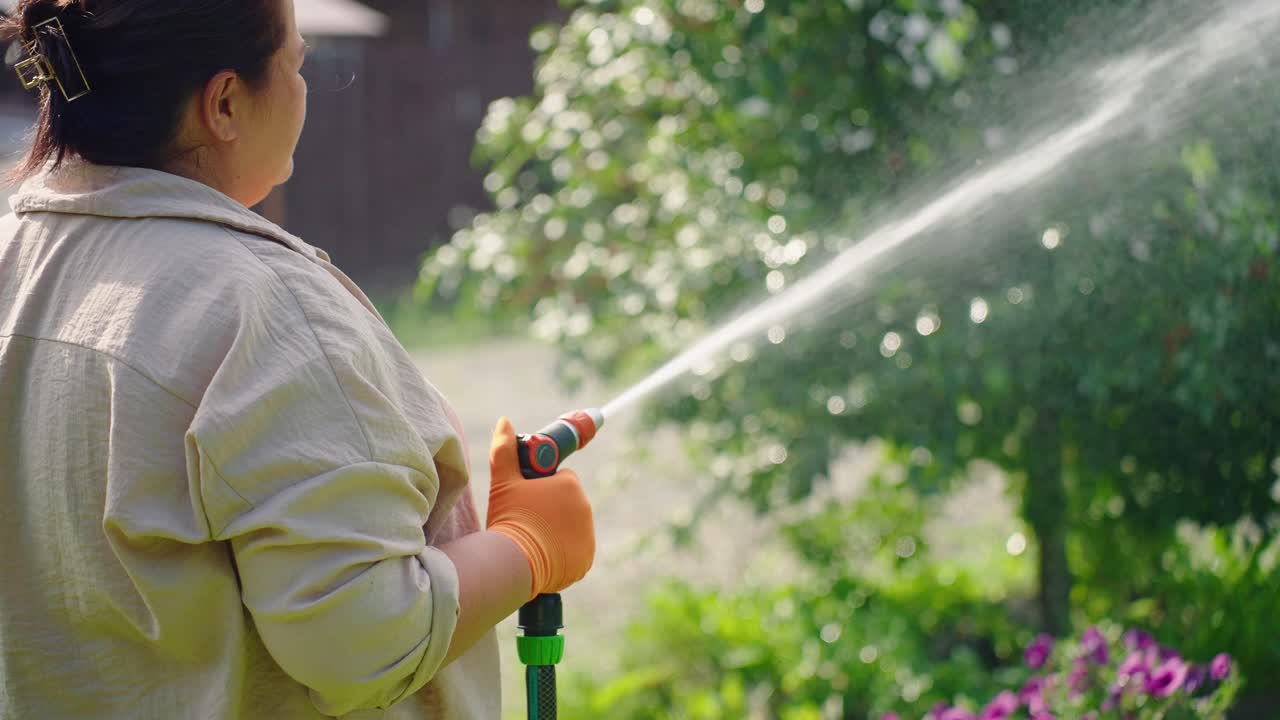 Un giardiniere che si prende cura del verde con un tubo, godendosi il caldo sole mentre spruzza acqua in una vivace scena di giardino con piante lussureggianti e sole splendente