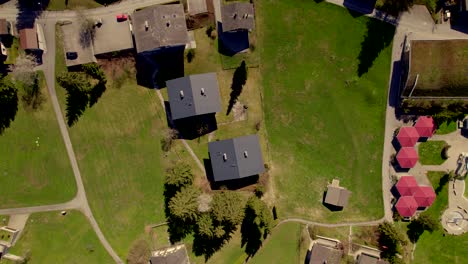 aerial-drone-footage-top-down-left-to-right-over-some-swiss-chalets,-swimming-pool-and-meadows-in-the-swiss-alps