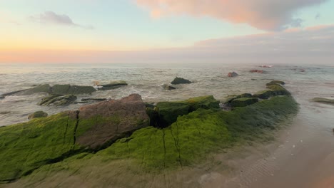 Ein-Ruhiger-Strand-Mit-Wellen,-Die-Am-Späten-Nachmittag-über-Felsen-Krachen