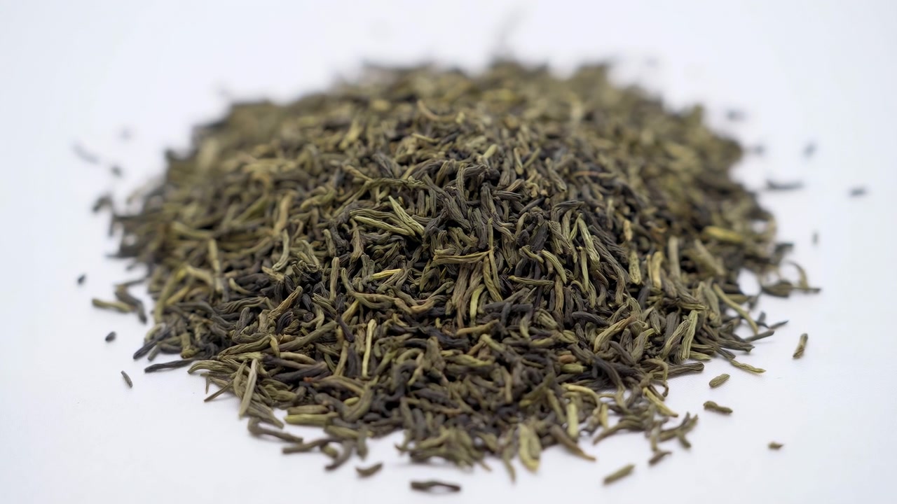 Close view of loose dried tea leaves resting on smooth white tabletop, with curled leaf strands, matte fibrous texture, soft shadows, neutral background, calm natural product display
