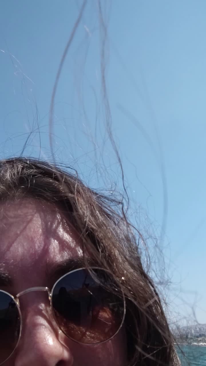 A woman with long hair is wearing sunglasses and looking at the camera, takes a selfie on a boat.