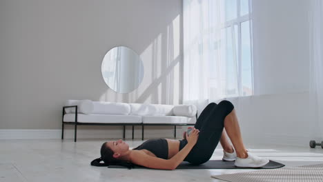 woman in sportswear doing hip bridge exercise. joyful attractive young woman lying on floor in living room and doing hip bridge exercise