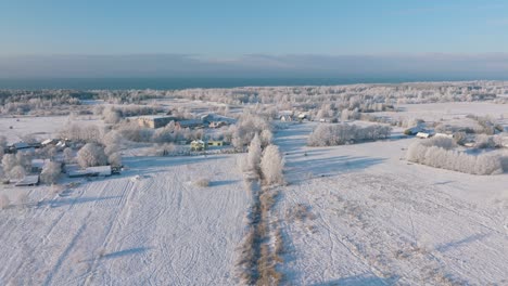 aerial establishing view of rural landscape in winter, snow covered countryside fields and trees, cold freezing weather, sunny winter day with blue sky, private houses, wide drone shot moving forward