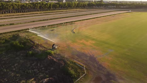 Orbitaufnahme-Eines-Leistungsstarken-Sprinklers,-Der-Das-Grüne-Gras-Der-Rennbahn-Von-San-Isidro,-Buenos-Aires,-Sonneneruption-Bewässert