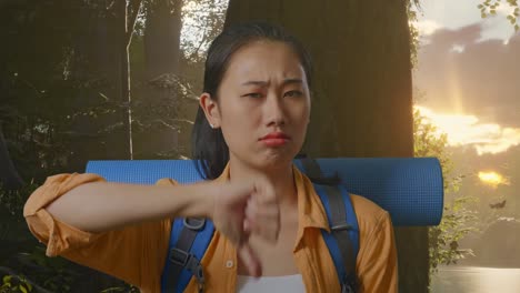 close up of asian female hiker with mountaineering backpack showing thumbs down gesture while exploring forest nature
