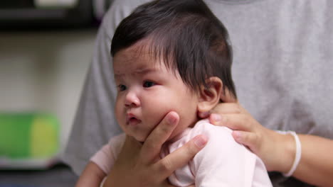 sitting on her mother's lap in a burping position, the new mom is holding the baby's head using both of her hands