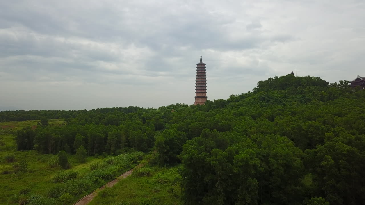 This frontal traveling shot captures the approach to the magnificent Bái Đính Pagoda in Ninh Binh, Vietnam, under a soft, cloudy sky. Witness the serene beauty of this important spiritual and cultural