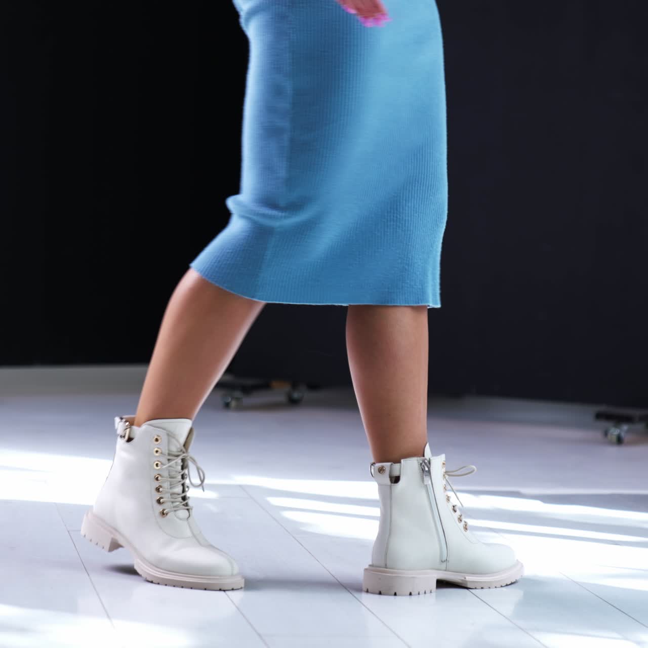 Female in blue midi dress walks by the room. Model demonstrating the boots made of leather, with tractor soles and laces