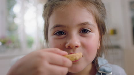 cute little girl eating cookie dipping biscuit into hot chocolate enjoying delicious treat at home in kitchen