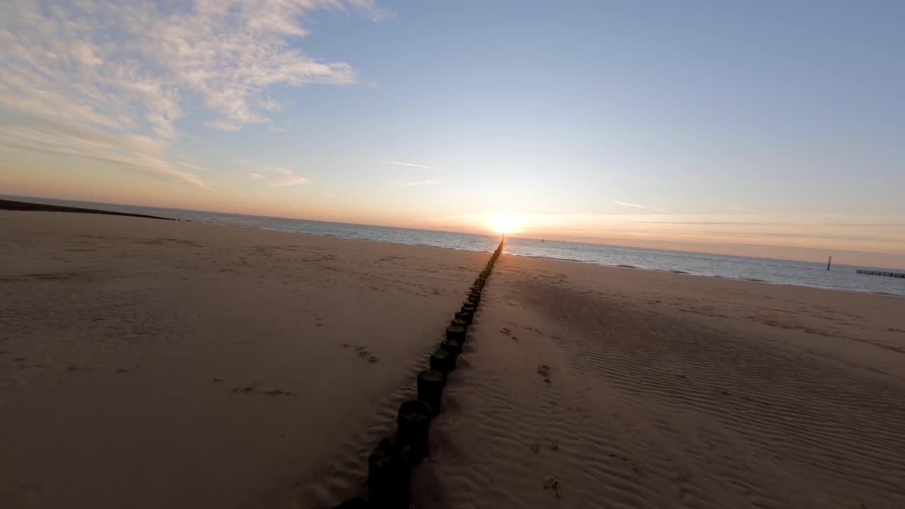 tiro rápido siguiendo una hilera de troncos de madera hacia la puesta de sol en una playa tranquila