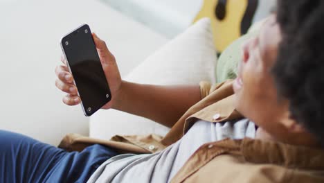 hombre afroamericano feliz usando un teléfono inteligente en casa