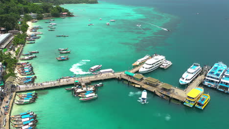 Tourists-disembark-koh-phi-phi-ferry-at-dock-passing-by-longtail-boats,-aerial-overview