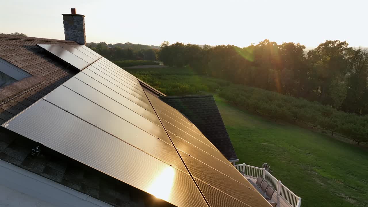 Reflecting sunlight on black photovoltaic units on rooftop of rural house. Aerial close up flyover. Scenic landscape of usa at golden sunset in fall season. Modern production of green energy