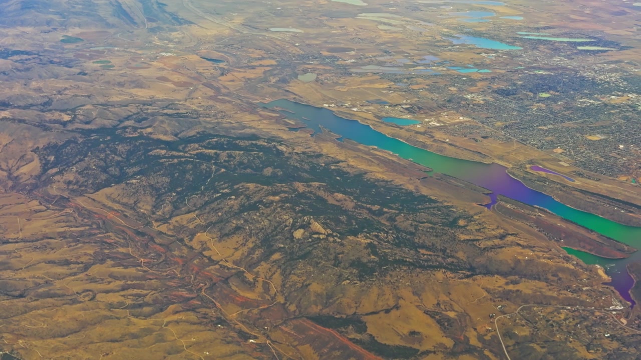 Río bajo, ancho y serpenteante junto a montañas poco profundas que bordean la expansión urbana de casas densas y campos agrícolas