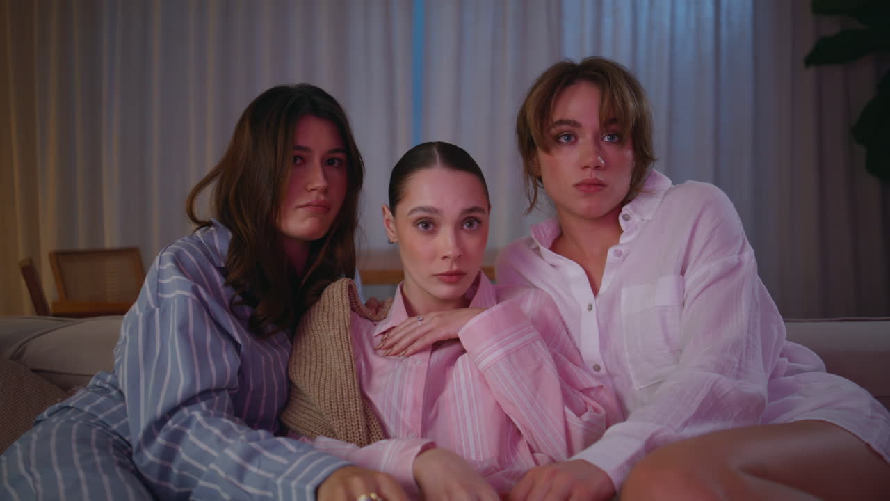 Girls shudder watching scary movie with popcorn at home couch night closeup