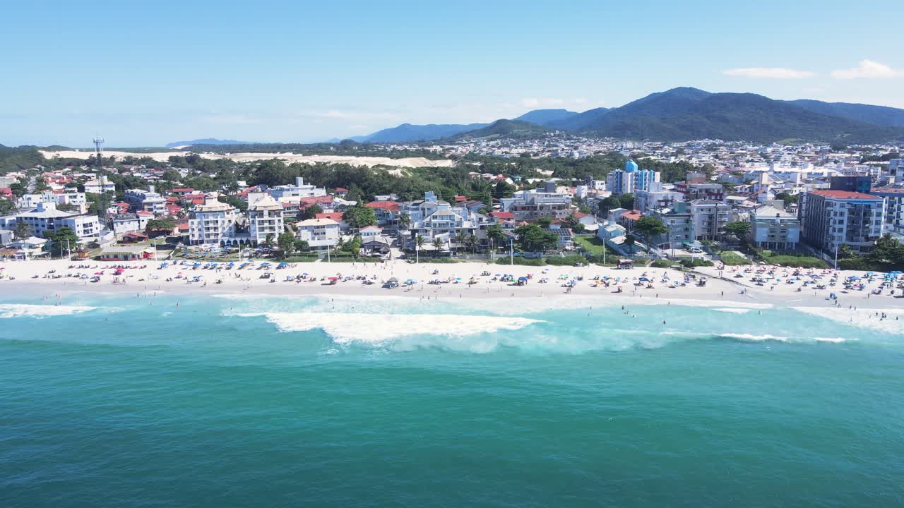 Panoramic aerial view of Ingleses beach in Florianópolis, Santa Catarina, crowded with people and umbrellas during the peak summer season with turquoise blue sea
