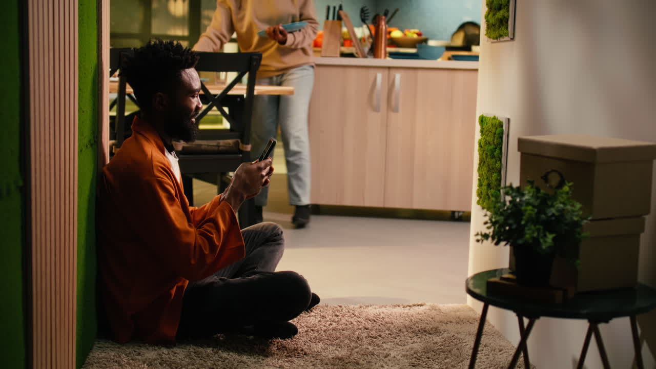 Afroamerikansk mand, alene hjemme, tekster på mobiltelefon i hyggelig entré