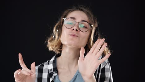 close up view of pleased woman in stylish glasses and headphones listening music with closed eyes and dancing over black background