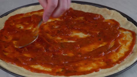 chef pouring pizza marinara on raw dough.