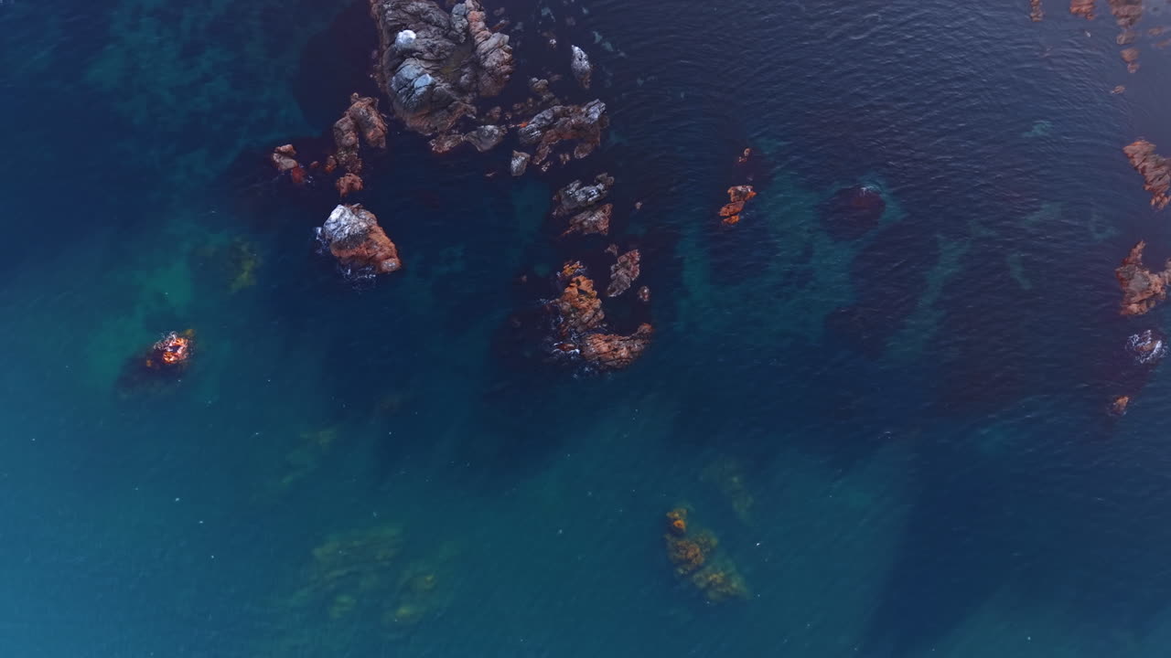 Rising over the wonderful blue waterscape. Some rocks stick out from water. Footage over the coast of the sea or ocean