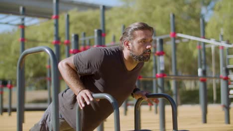 muscular athlete with disability doing push-ups on bars.