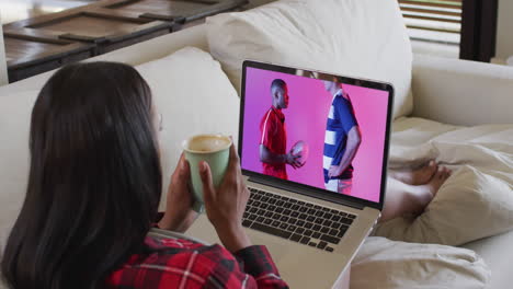 mujer biracial viendo una computadora portátil con un jugador de rugby masculino diverso con la pelota en la pantalla