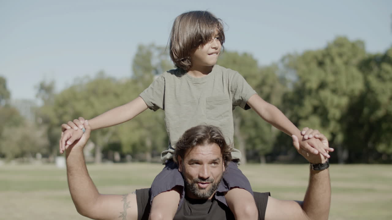 hijo feliz sentado en los hombros de papá en un soleado día de verano
