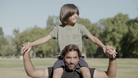 happy son sitting on dads shoulders on sunny summer day