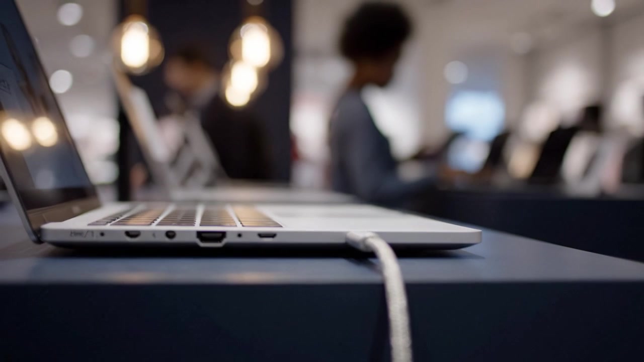 A close-up view of a modern laptop charging in a sleek retail environment, blending technology and design aesthetics under warm ambient lighting.