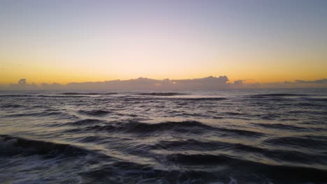 Drone-shot-flying-low-over-a-beach-and-low-over-waves-towards-the-ocean-during-sunrise-in-Cariló,-Argentina