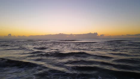 drone shot flying low over a beach and low over waves towards the ocean during sunrise in cariló, argentina
