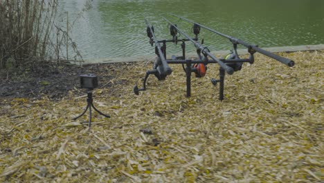 drone rotating shot of black carp fishing rods with carp bite indicators and reels set up on a rod pod on a lake in a background at daytime