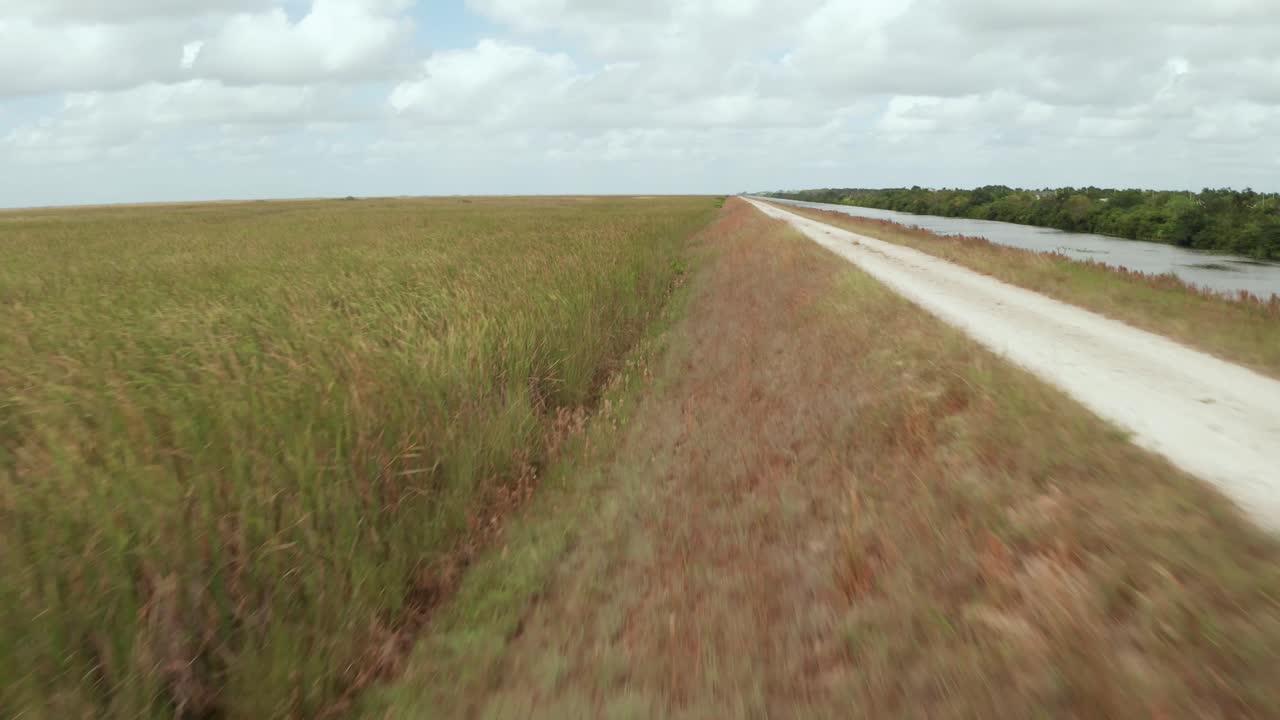Drone shot of Dirt Road and Sawgrass in the Florida Everglades, close to Sawgrass next to the Levee. Moving Forward, Boom up and pan right to reveal the Sawgrass Expressway and Neighborhoods