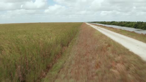 drone tiro de carretera de tierra y sawgrass en los everglades de florida, cerca de sawgrass al lado del dique. moviéndose hacia adelante, boom y pan a la derecha para revelar la autopista sawgrass y los vecindarios