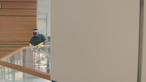 distant view of cleaning man wearing gloves cleaning stair railing inside an office building