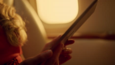 woman watching green tablet screen on airplane trip. hands holding pad closeup