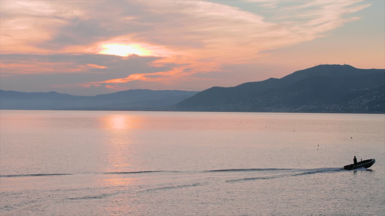 석양에 왼쪽에서 오른쪽으로 움직이는 작은 배, 배경에는 산이 있고 주황색 하늘은 포르토피노 근처에서 촬영됩니다.