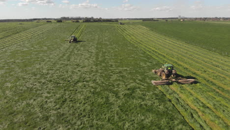 aerial ascending rotation around two tractor mowers working the same paddock field