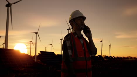 engineer talking on phone at wind farm and solar panel farm sunset