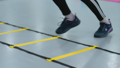 leg view of person in black sneakers and joggers performing agility drills on a speed ladder, focusing on stamina and endurance training with rapid in-and-out footwork for improved coordination