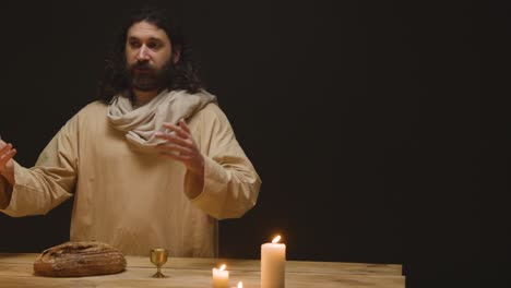 scatto in studio di un uomo che indossa abiti con capelli lunghi e barba che rappresenta la figura di gesù cristo che benedice il pane e il vino